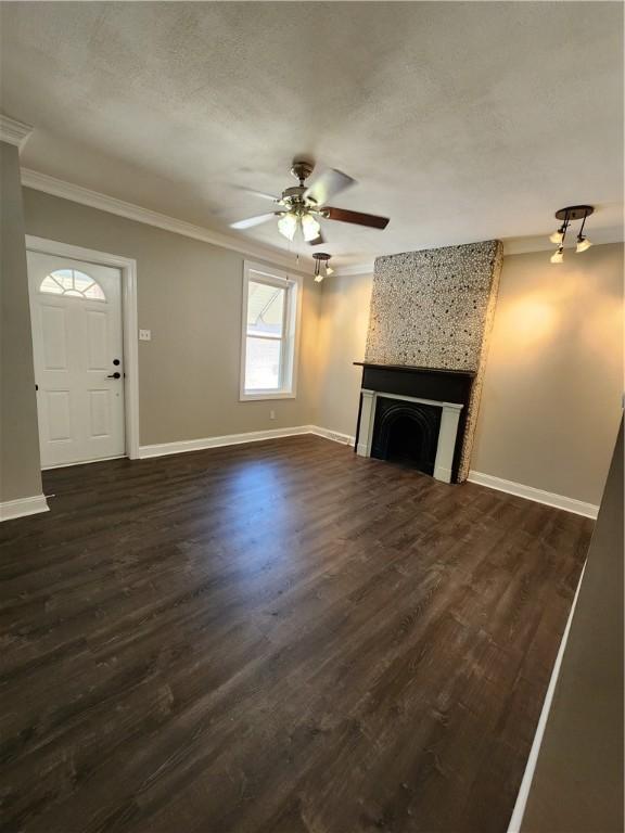 unfurnished living room with crown molding, a large fireplace, dark wood-type flooring, and ceiling fan