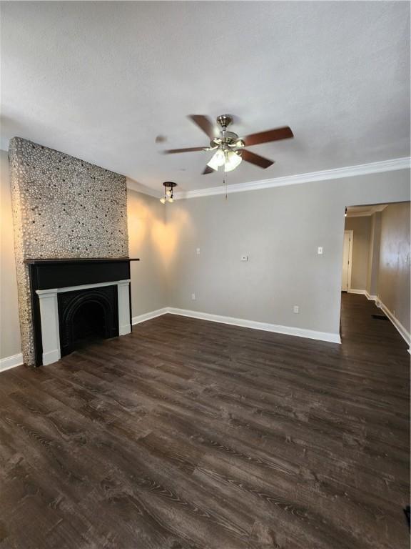 unfurnished living room with a textured ceiling, ornamental molding, dark hardwood / wood-style flooring, a large fireplace, and ceiling fan