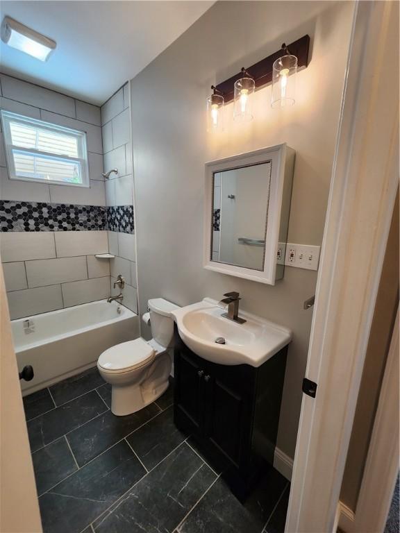 full bathroom featuring vanity, tiled shower / bath combo, and toilet