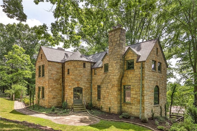 tudor home featuring entry steps, a chimney, a high end roof, and a front yard