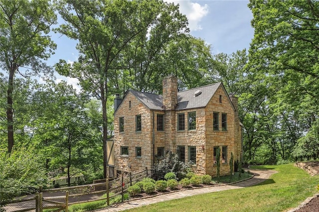 view of front of property with stone siding, a chimney, fence, and a front yard