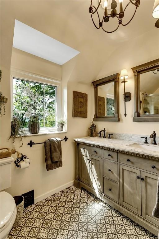 bathroom with a notable chandelier, vanity with extensive cabinet space, dual sinks, toilet, and tile floors