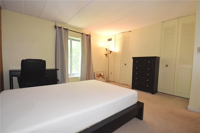 bedroom featuring light colored carpet and two closets