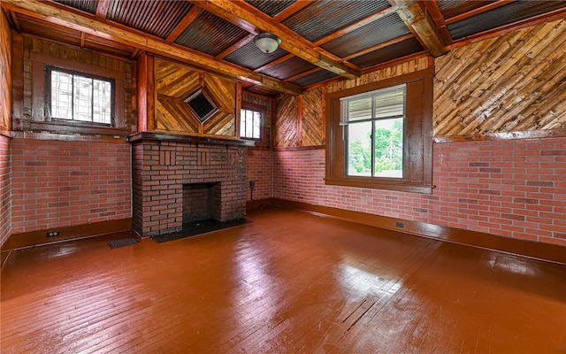 unfurnished living room with brick wall, a brick fireplace, coffered ceiling, hardwood / wood-style floors, and wooden walls