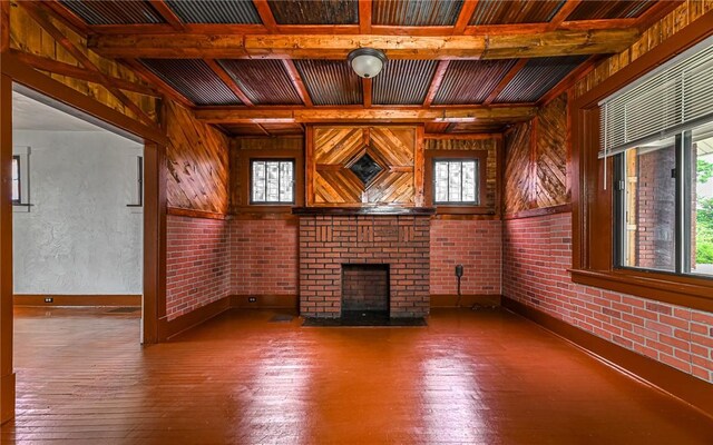 unfurnished living room with a wealth of natural light, wood walls, a brick fireplace, and dark hardwood / wood-style floors