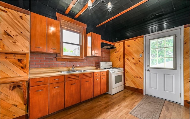 kitchen with wooden walls, ventilation hood, sink, white range with gas stovetop, and light hardwood / wood-style flooring