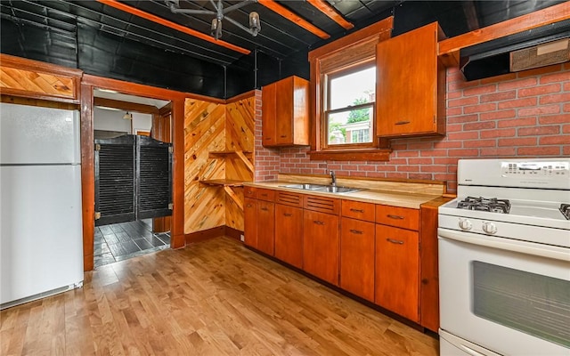 kitchen featuring brick wall, range hood, sink, light wood-type flooring, and white appliances