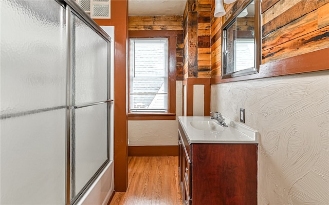 bathroom with enclosed tub / shower combo, hardwood / wood-style flooring, plenty of natural light, and vanity with extensive cabinet space