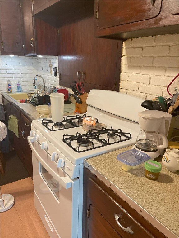 kitchen with gas range gas stove, dark brown cabinetry, sink, and light tile flooring