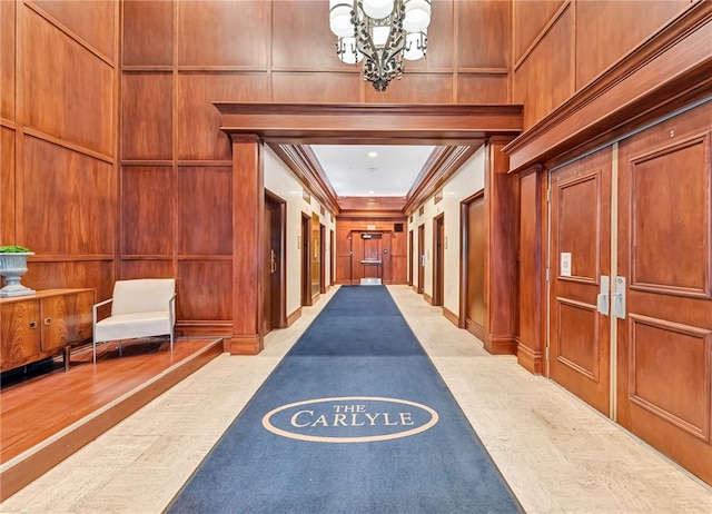 corridor with crown molding, an inviting chandelier, wooden walls, and light hardwood / wood-style flooring