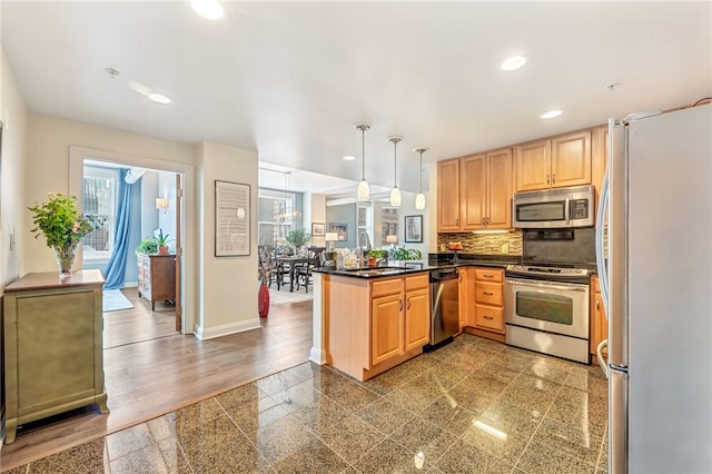 kitchen featuring hanging light fixtures, appliances with stainless steel finishes, kitchen peninsula, backsplash, and sink