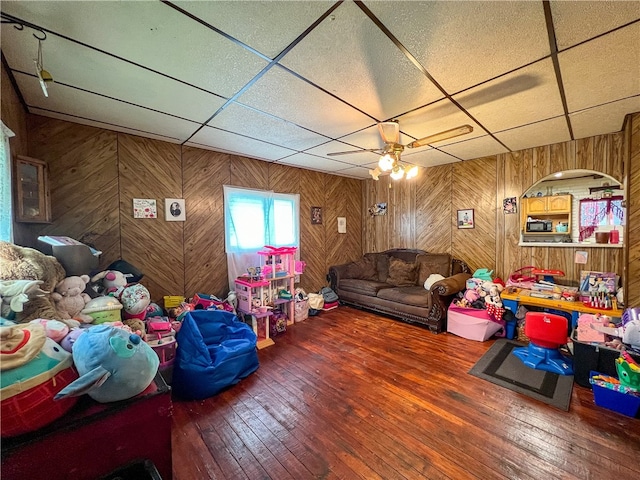 living room featuring hardwood / wood-style flooring, ceiling fan, wood walls, and a drop ceiling