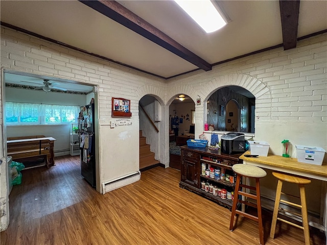 hall with brick wall, baseboard heating, hardwood / wood-style flooring, and beam ceiling