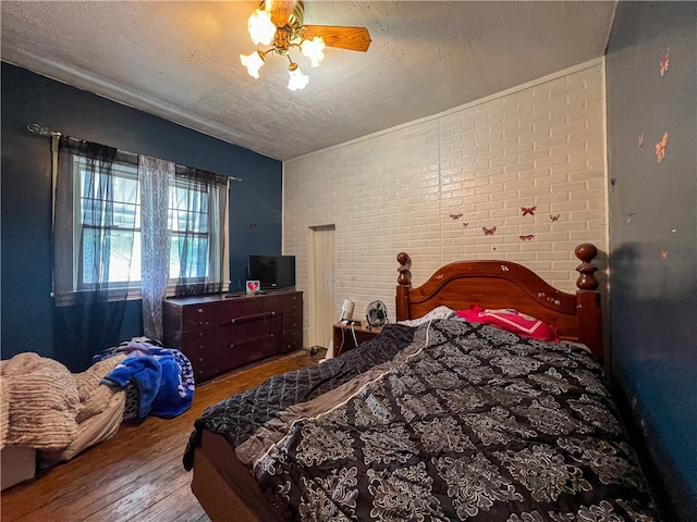 bedroom featuring brick wall, wood-type flooring, ceiling fan, and a textured ceiling