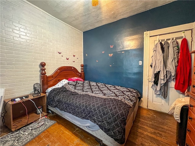 bedroom featuring dark hardwood / wood-style floors, a textured ceiling, and brick wall