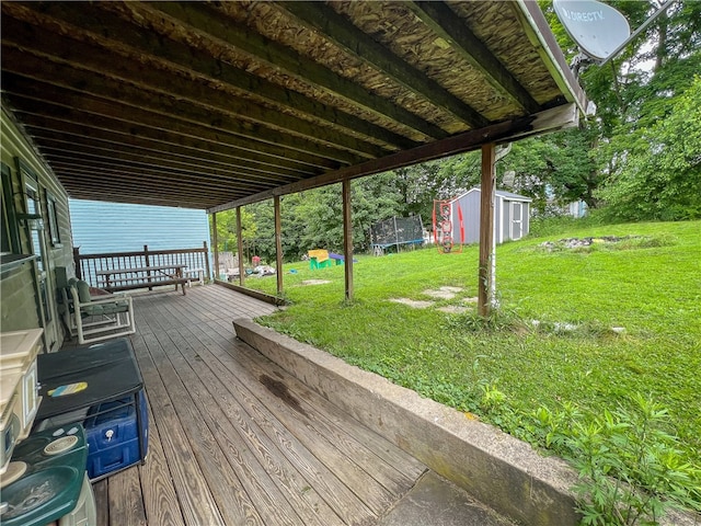 wooden deck featuring a lawn, a trampoline, and a storage shed