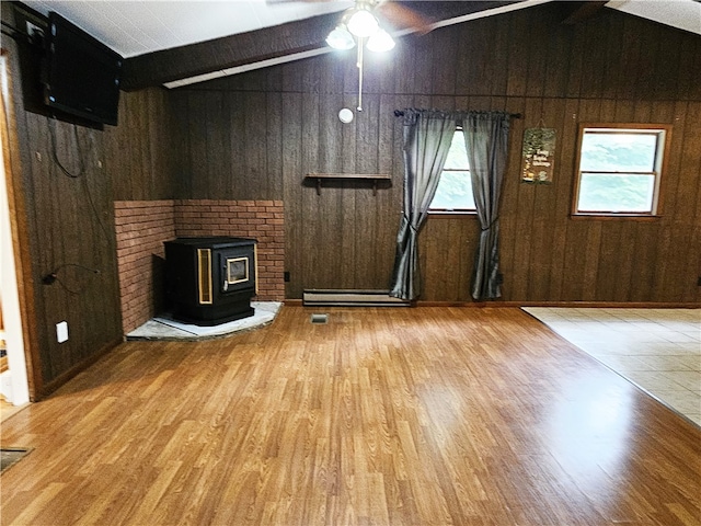 unfurnished living room featuring a healthy amount of sunlight, wood walls, and a wood stove