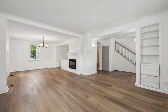 unfurnished living room with a notable chandelier, hardwood / wood-style flooring, built in features, and ornamental molding