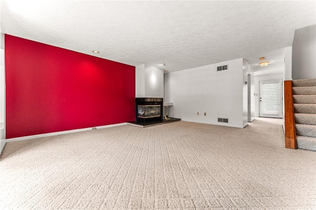 unfurnished living room with carpet flooring, a textured ceiling, and a multi sided fireplace