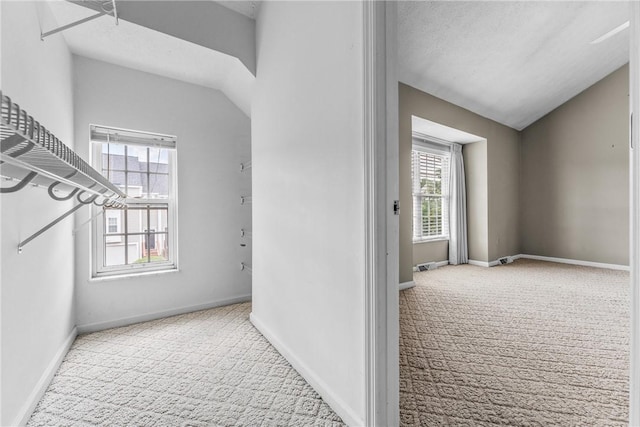 hallway with lofted ceiling, light colored carpet, and a textured ceiling