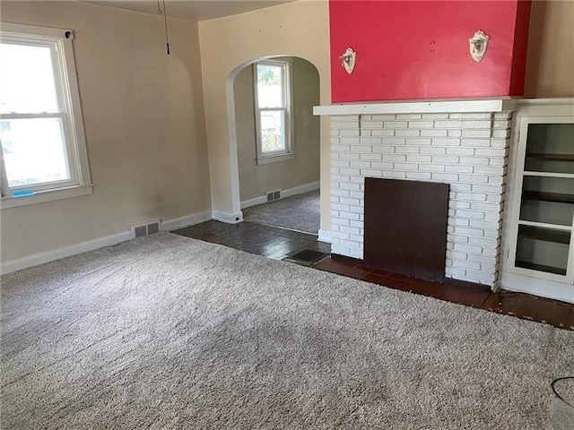 unfurnished living room featuring a wealth of natural light, dark colored carpet, and a fireplace