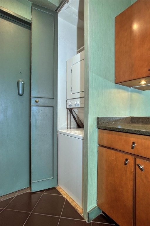 laundry room featuring stacked washing maching and dryer and dark tile patterned floors