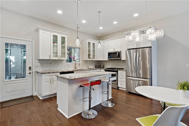 kitchen with white cabinets, stainless steel appliances, a kitchen island, and hanging light fixtures