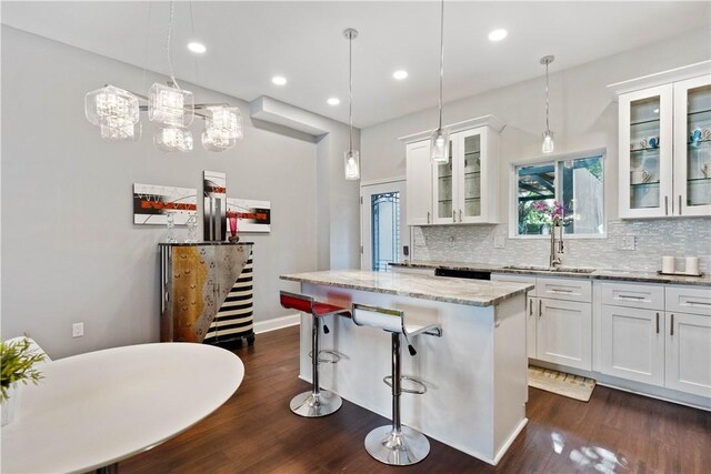 kitchen with white cabinetry, pendant lighting, a kitchen island, and light stone countertops