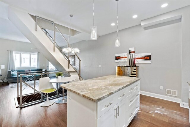 kitchen featuring white cabinetry, a center island, light stone counters, hardwood / wood-style floors, and pendant lighting