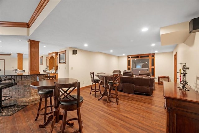 dining room with ornate columns, wood-type flooring, indoor bar, and ornamental molding