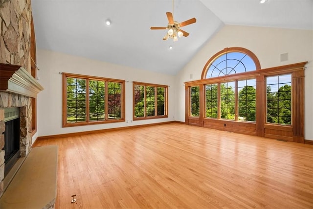 unfurnished living room with a stone fireplace, ceiling fan, light hardwood / wood-style flooring, and high vaulted ceiling