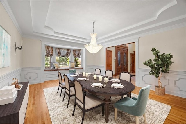 dining space with a notable chandelier, light hardwood / wood-style floors, a raised ceiling, and crown molding