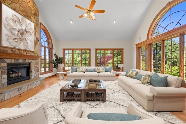 living room featuring ceiling fan, a healthy amount of sunlight, a stone fireplace, light hardwood / wood-style flooring, and high vaulted ceiling