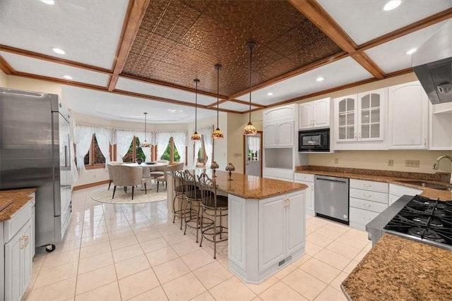 kitchen featuring appliances with stainless steel finishes, dark stone counters, a kitchen island, white cabinetry, and hanging light fixtures