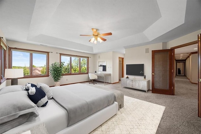 bedroom featuring ceiling fan, a raised ceiling, and light carpet