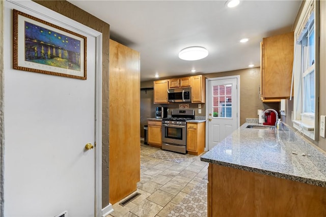 kitchen featuring stainless steel appliances, light stone countertops, and sink