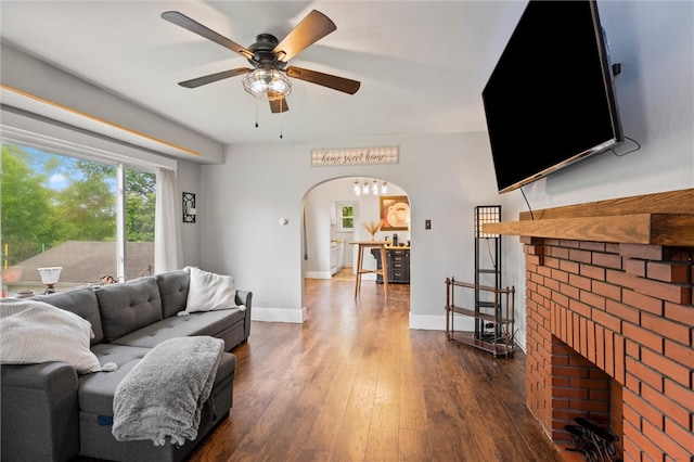 living room featuring a brick fireplace, ceiling fan, and dark wood-type flooring