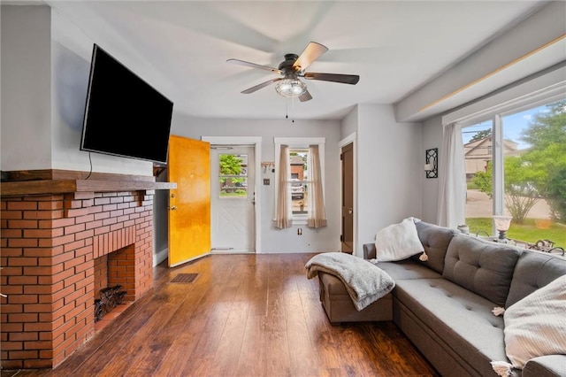 living room featuring dark hardwood / wood-style floors, ceiling fan, and a brick fireplace