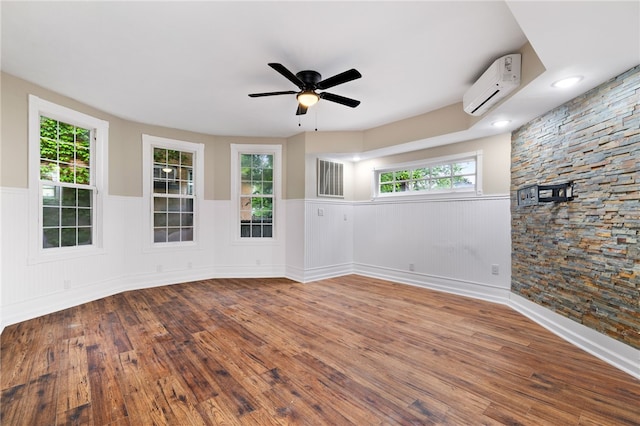 empty room featuring ceiling fan, a healthy amount of sunlight, wood-type flooring, and a wall mounted AC