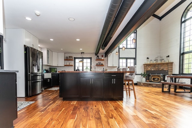 kitchen with black fridge, white cabinets, a fireplace, and light hardwood / wood-style floors