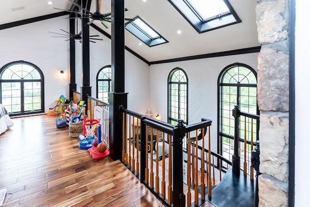 hallway with high vaulted ceiling, ornamental molding, hardwood / wood-style flooring, and a skylight