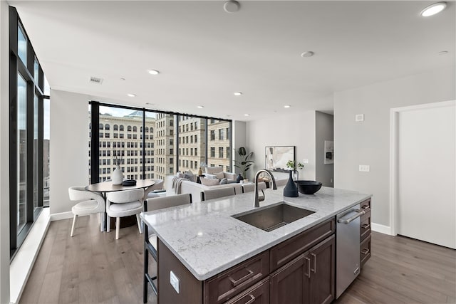 kitchen with hardwood / wood-style flooring, a kitchen island with sink, light stone countertops, a wall of windows, and sink