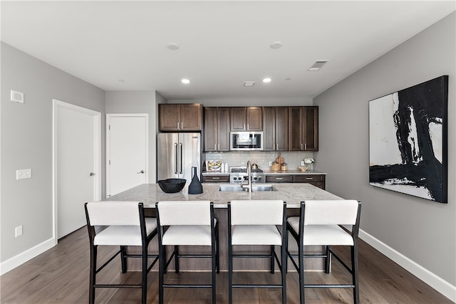 kitchen with dark hardwood / wood-style floors, backsplash, a kitchen island with sink, and appliances with stainless steel finishes