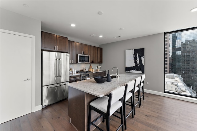 kitchen with a kitchen breakfast bar, an island with sink, dark wood-type flooring, light stone counters, and high quality appliances