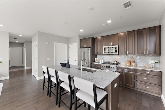 kitchen featuring tasteful backsplash, dark wood-type flooring, premium appliances, and a center island with sink