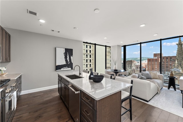 kitchen with dark hardwood / wood-style floors, a wall of windows, a kitchen bar, sink, and a kitchen island with sink