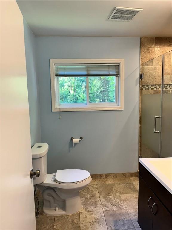 bathroom with a wealth of natural light, a shower with door, vanity, and toilet