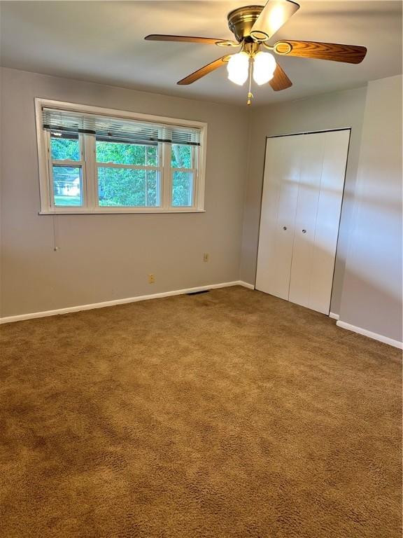 unfurnished bedroom featuring ceiling fan, a closet, and dark colored carpet