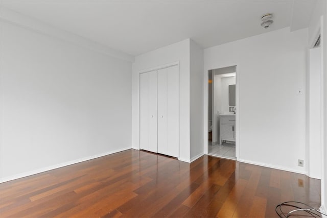 unfurnished bedroom featuring ensuite bathroom, a closet, and wood-type flooring