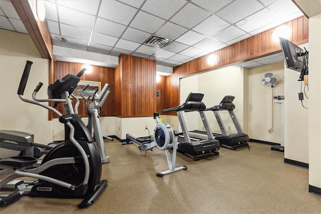 gym featuring a paneled ceiling and wooden walls